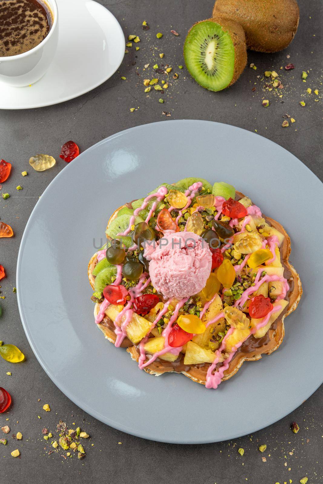 Heart waffle with kiwi and pineapple with gummy candy and ice cream on it.