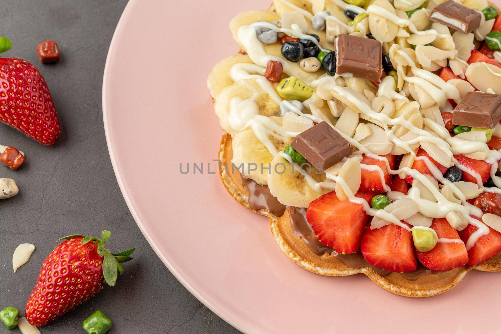 Heart waffle with banana and strawberry with gummy candy and ice cream on it.