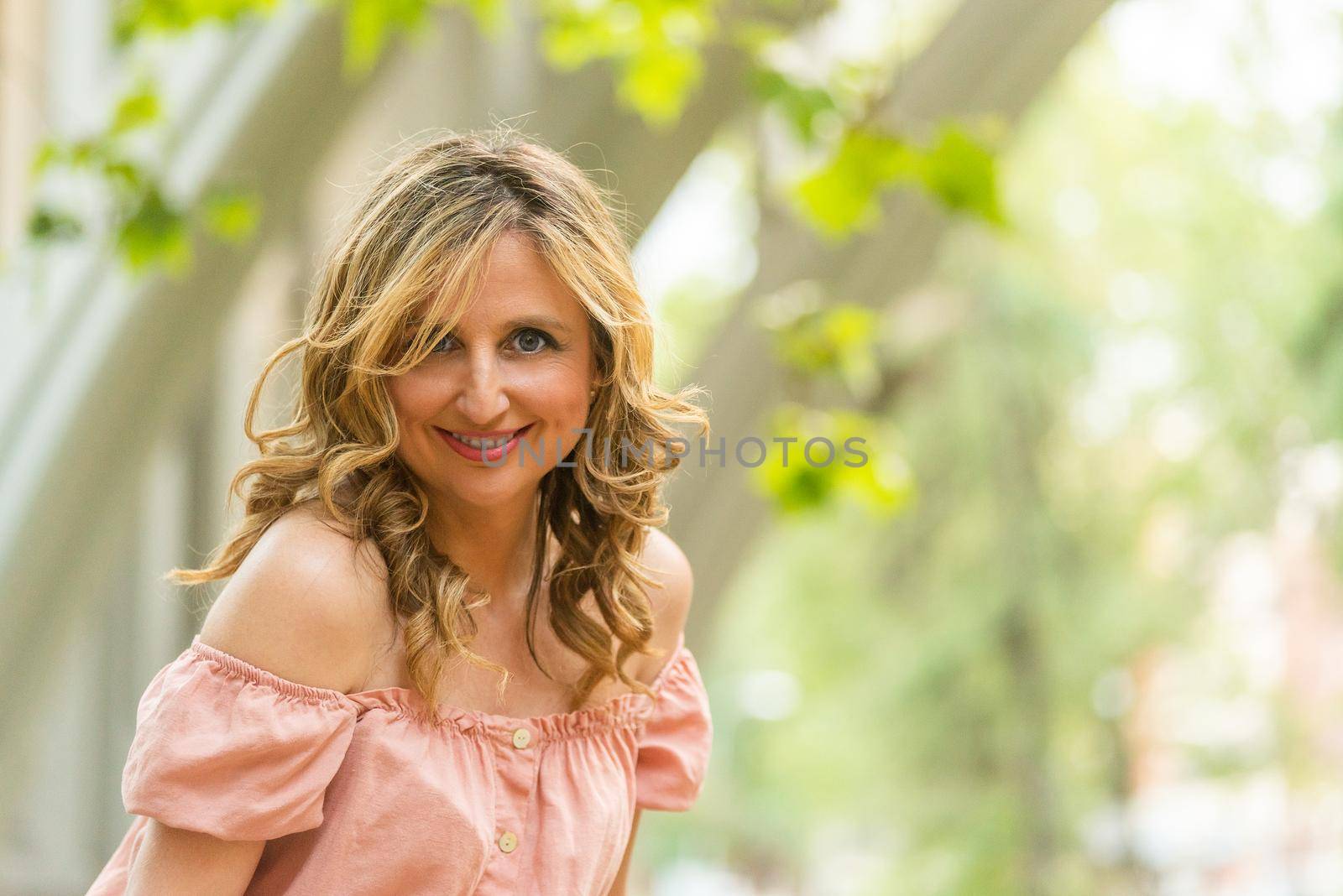 Portrait of happy mature woman with trees background. Middle aged woman in the city looking at camera.