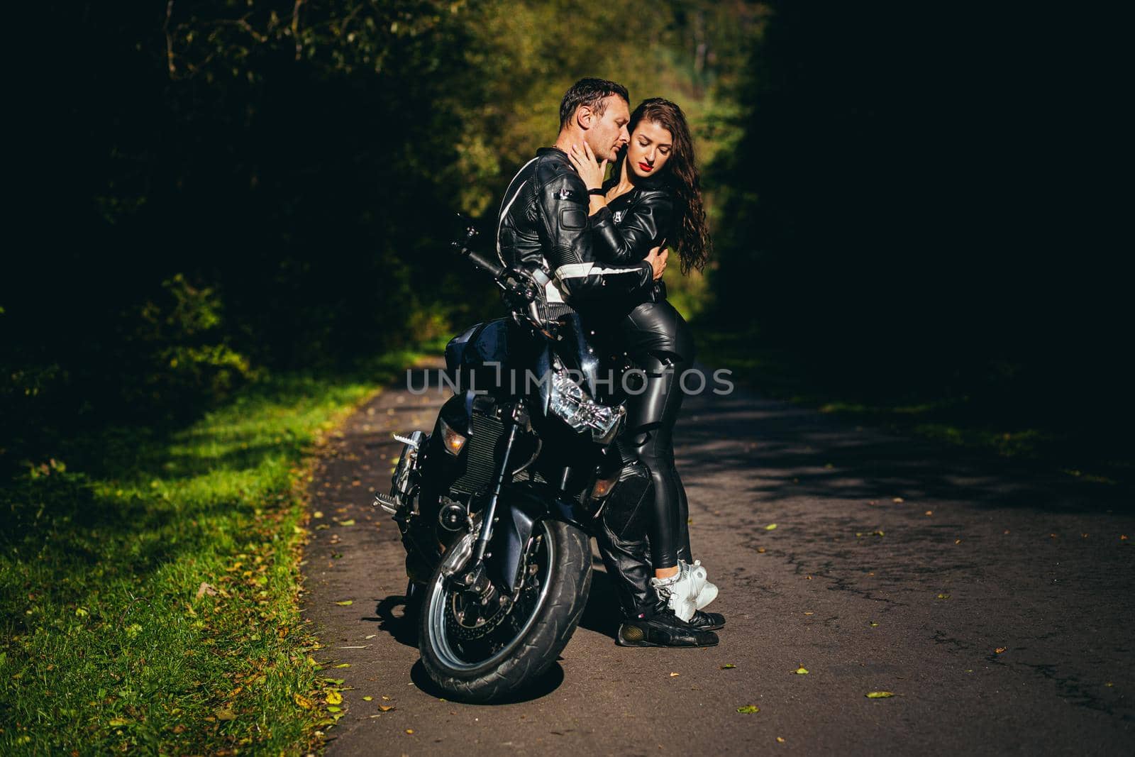 Handsome young man and beautiful young girl, couple sitting on a motorcycle, standing near a motorcycle in black leather clothes, hugging, in nature, on the street by voronaman