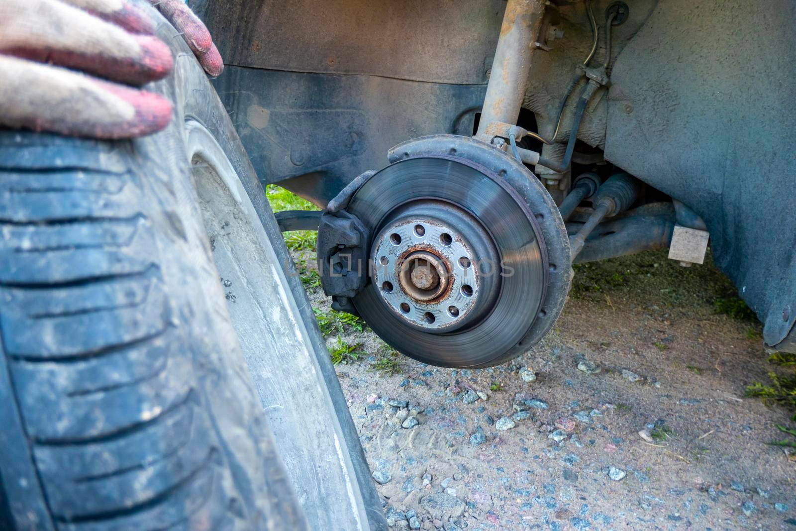 Tire wheel with missing cap cover on parked car with man replacing hubcap with new shiny metal outside. High quality photo