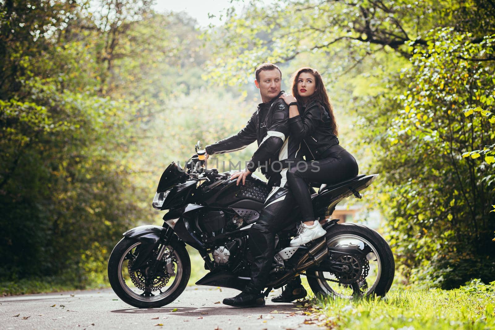 Handsome young man and beautiful young girl, couple sitting on a motorcycle, standing near a motorcycle in black leather clothes, hugging, in nature, on the street by voronaman