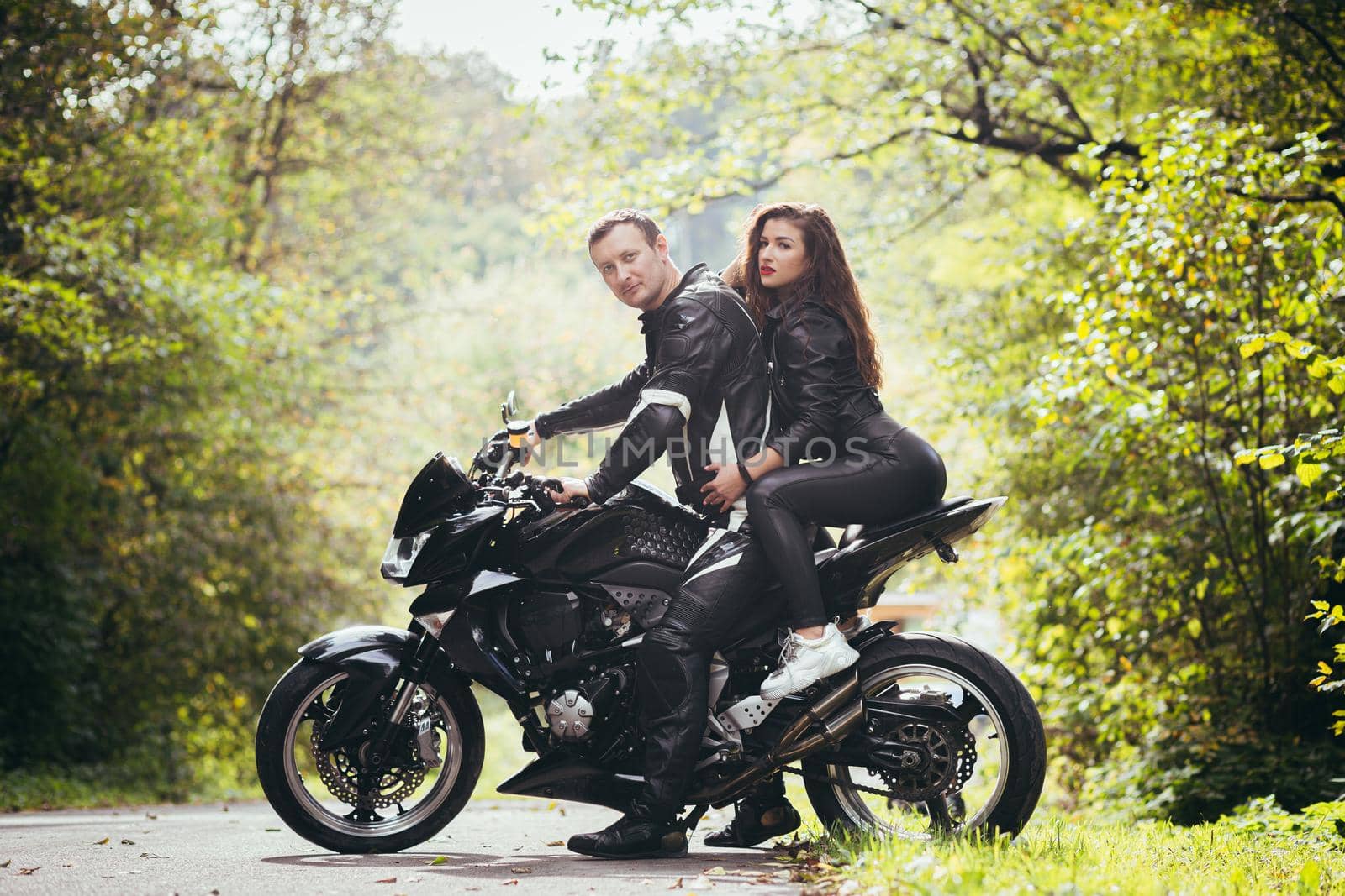 Handsome young man and beautiful young girl, couple sitting on a motorcycle, standing near a motorcycle in black leather clothes, hugging, in nature, on the street by voronaman