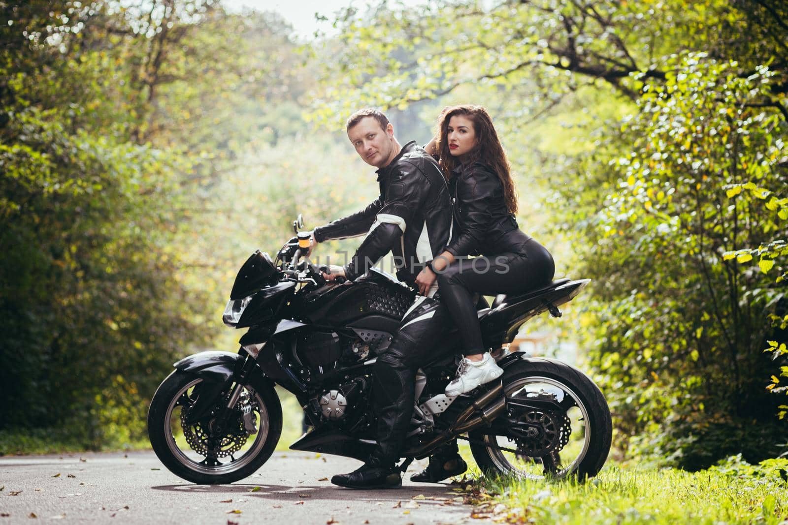 Handsome young man and beautiful young girl, couple sitting on a motorcycle, standing near a motorcycle in black leather clothes, hugging, in nature, on the street by voronaman