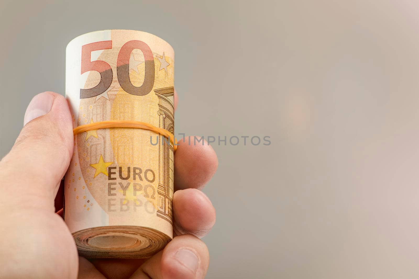 The hand holds a roll of 50 euro banknotes. Euro banknotes rolled up in a white man's hand on a gray background. The concept of financial assistance, real estate purchase, loan or insurance payment