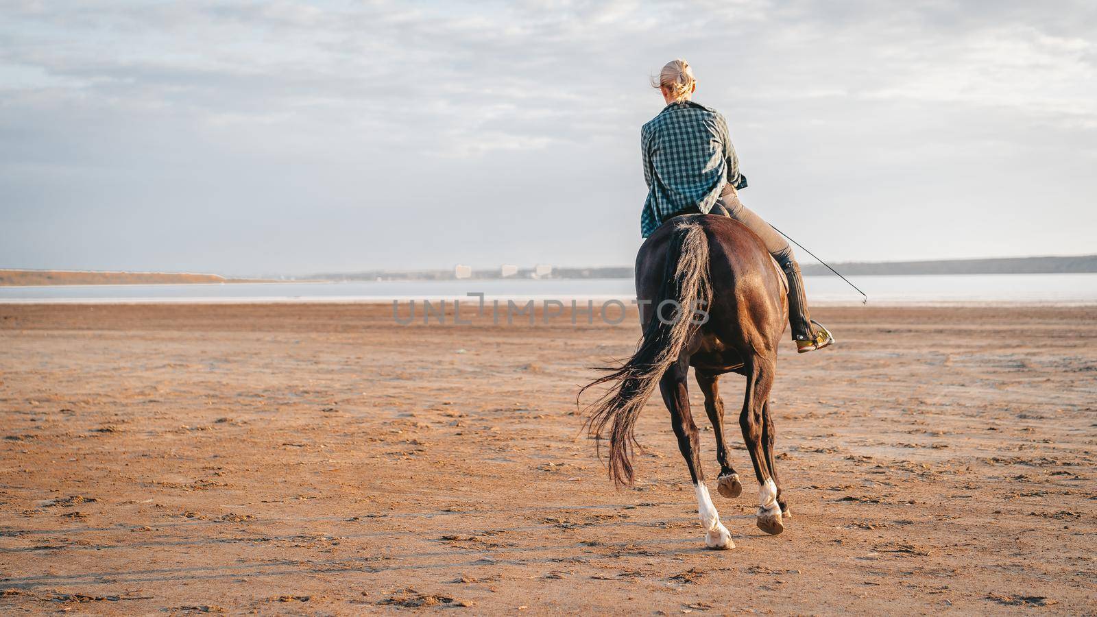 Woman rides horse on beautiful autumn nature landscape by river or lake. Concept of farm animals, training, horse racing.