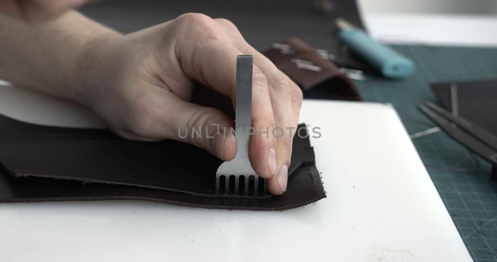 Close up men's hands make a leather product. Punching holes in the leather with a hole punch with a hammer. Tools for leather craft. by vovsht