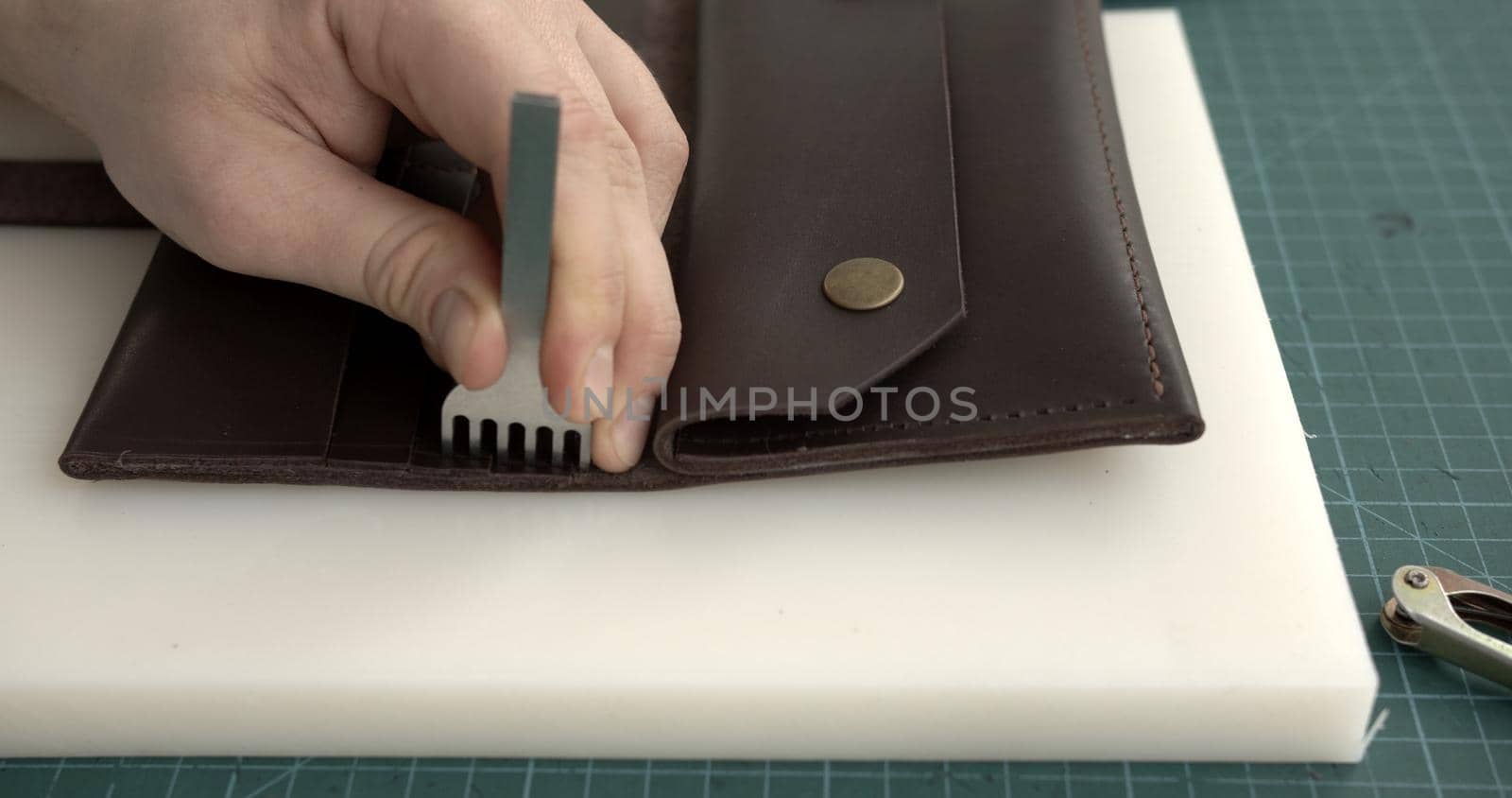 Craftsman making holes in leather with puncher tool. Working process with a brown natural leather. by vovsht