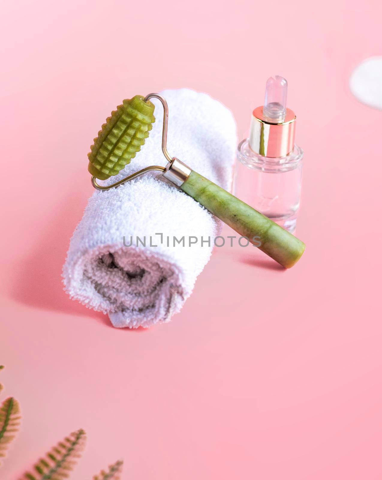 Jade Roller to Eliminate Eye Puffiness, Wrinkles and Relax Muscles. Jade Stone Face Massager, Neck, Skin Care Routine. texture massager massager with spikes for face in green color on pink background
