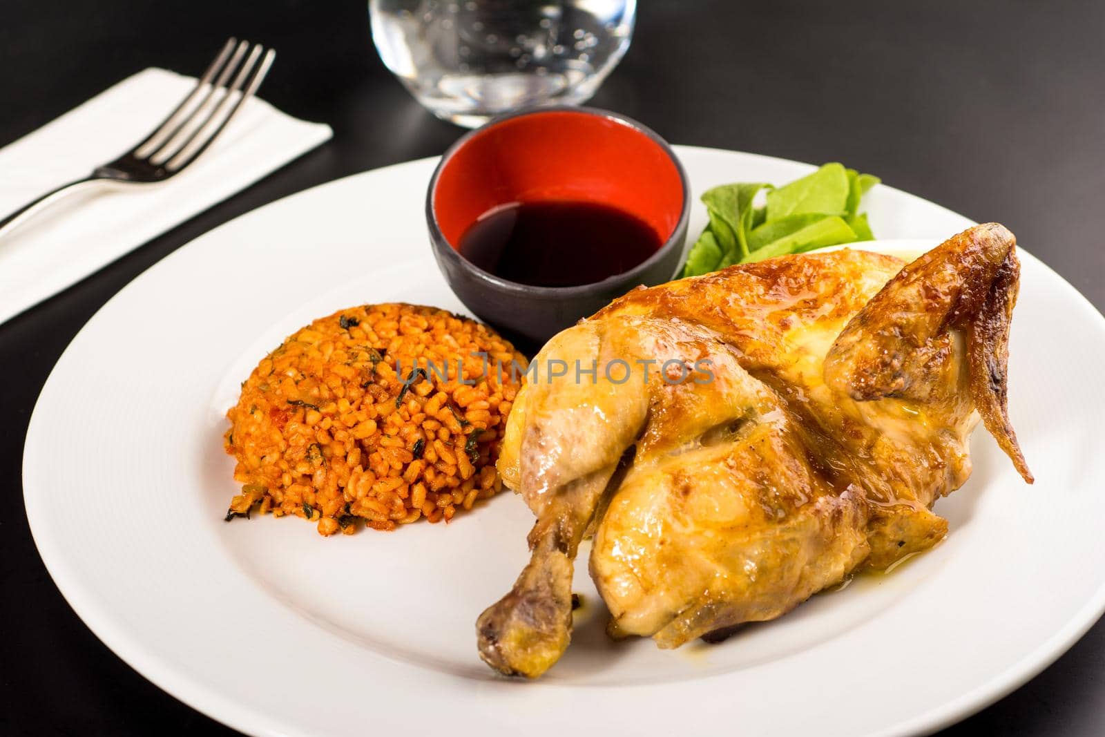 Roasted chicken cooked on charcoal with bulgur pilaf on a white porcelain plate.