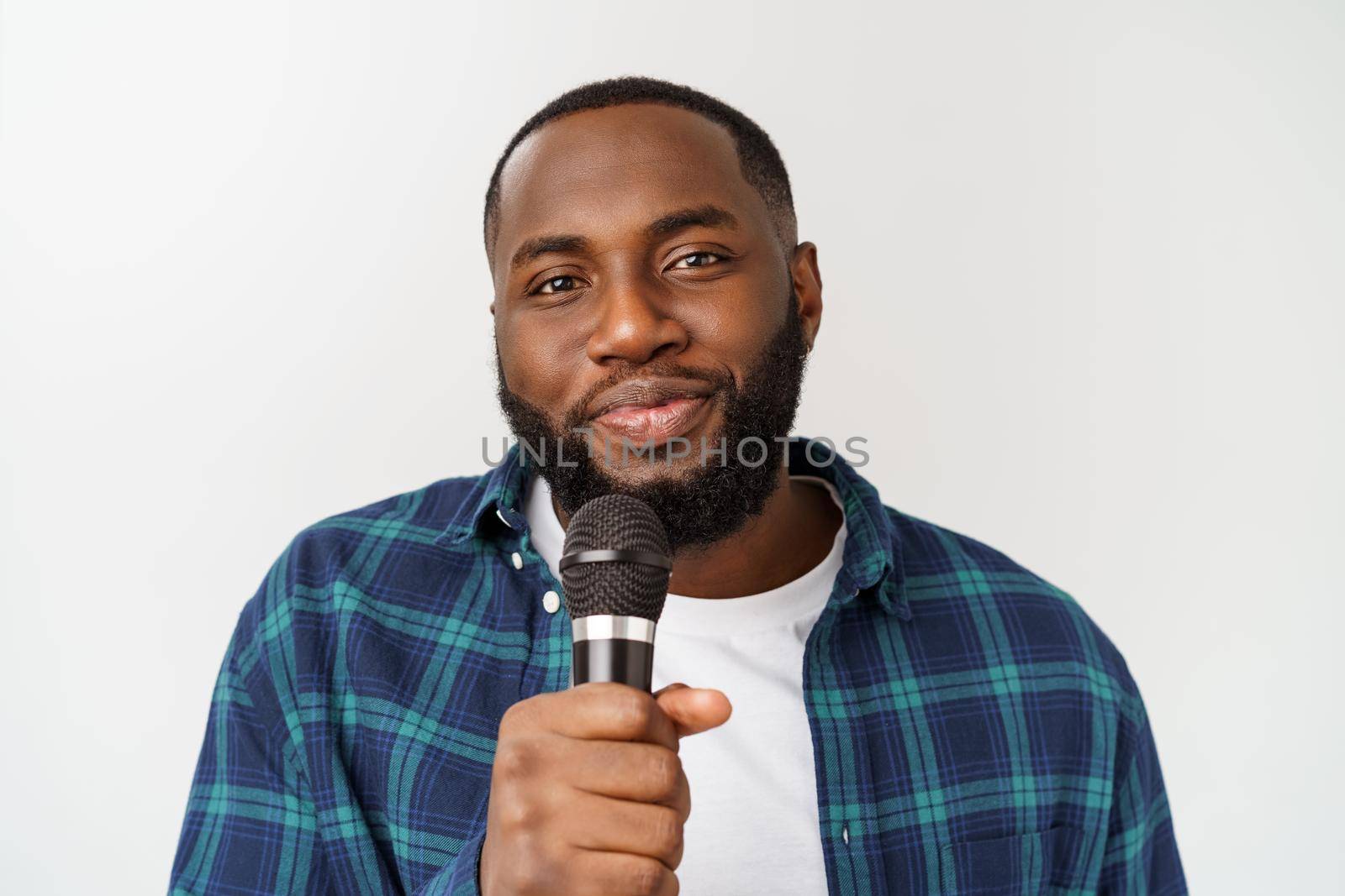 Portrait of cheerful positive chic handsome african man holding microphone singing song. Isolated on white background. by Benzoix