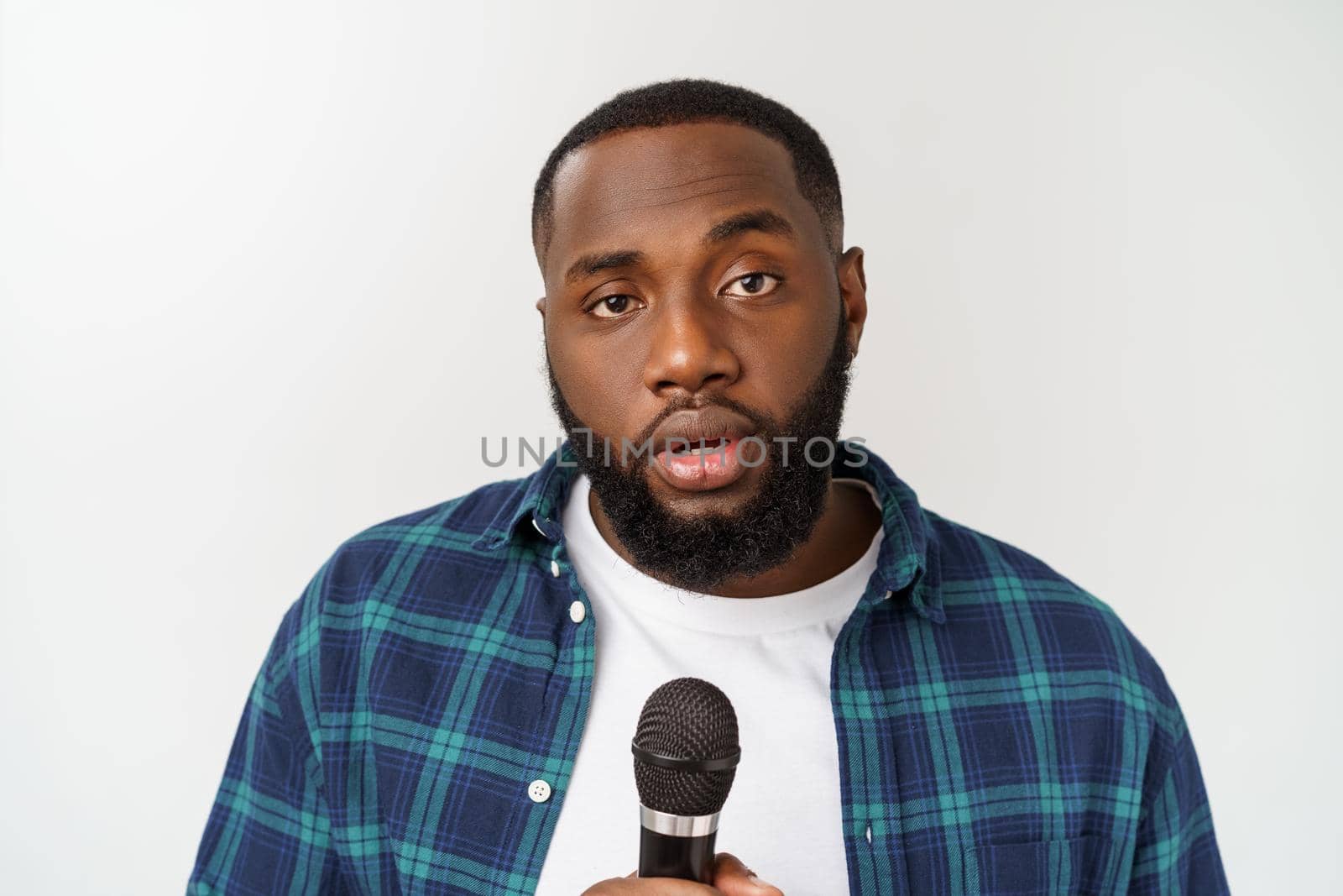 Portrait of cheerful positive chic handsome african man holding microphone singing song. Isolated on white background. by Benzoix