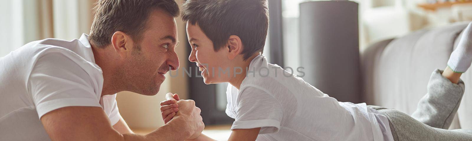 Merry man is fighting hands with little boy while having fun on floor in living room