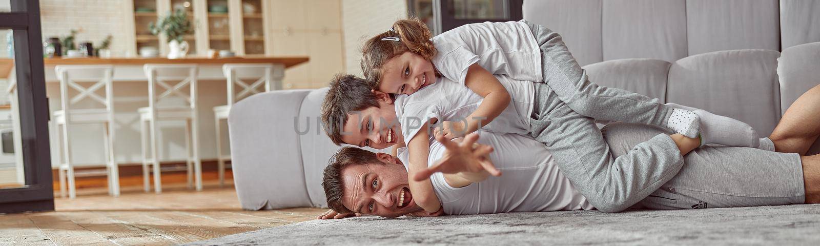 Funny dad with kids on back in living room by Yaroslav_astakhov