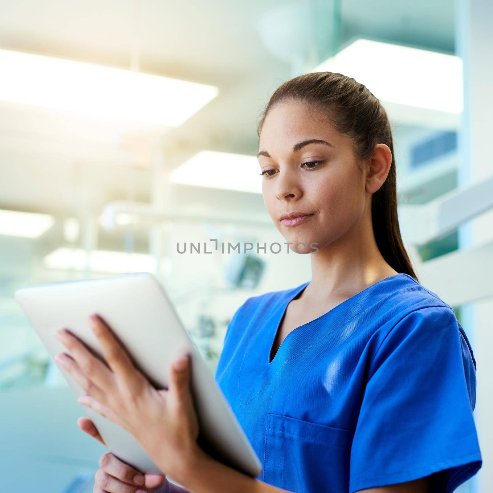 Using the latest technology to her patients benefit. a young nurse using a tablet while standing inside a clinic. by YuriArcurs