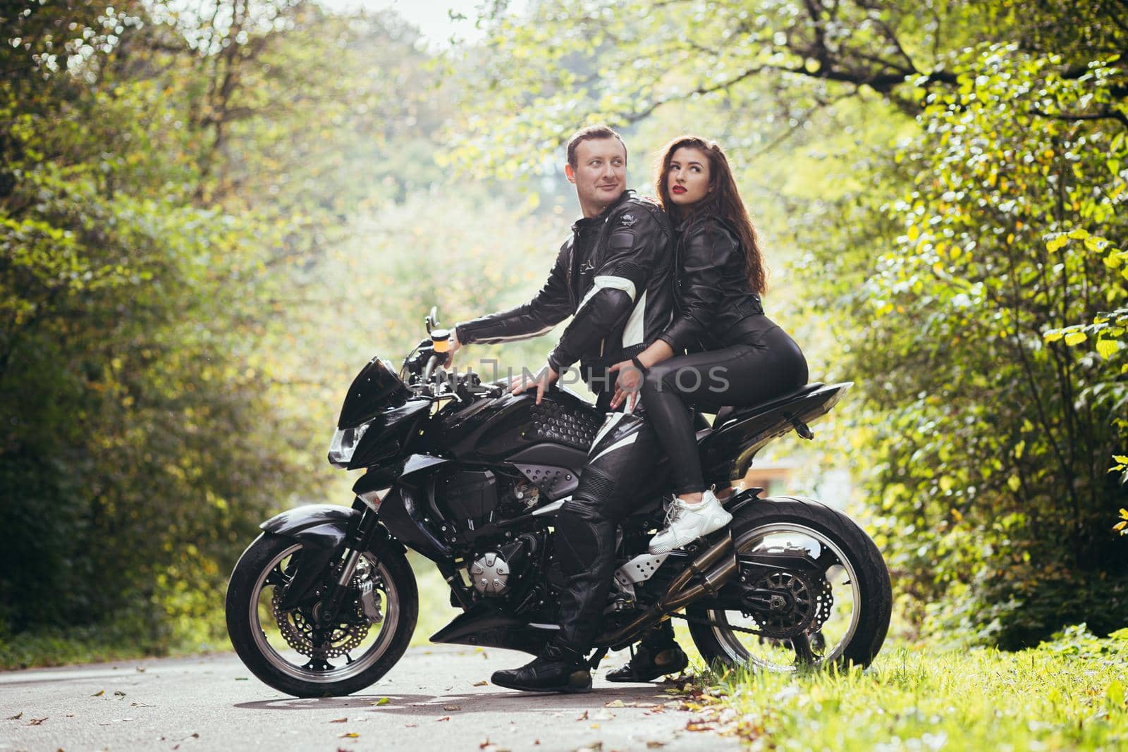 Handsome young man and beautiful young girl, couple sitting on a motorcycle, standing near a motorcycle in black leather clothes, hugging, in nature, on the street by voronaman