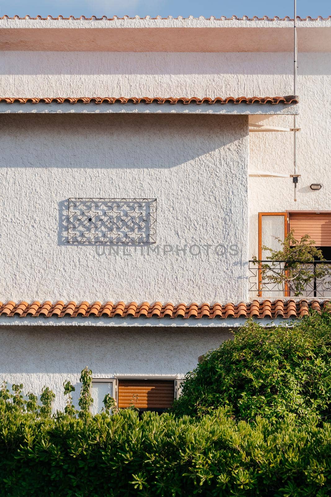 Typical white house facade part in italian city near the sea. Brown windows on white wall. Mediterranean village style architecture.