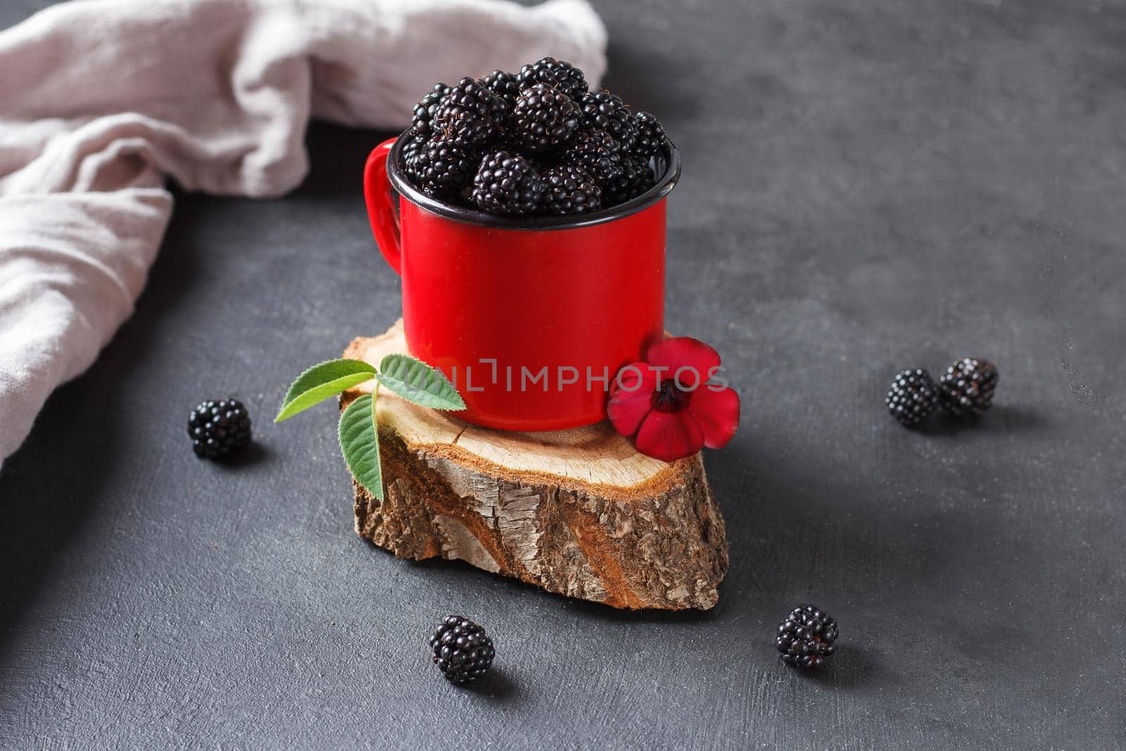 Fresh blackberry in a mug on a wooden stand on a black background with a flower. The concept of natural food. by lara29