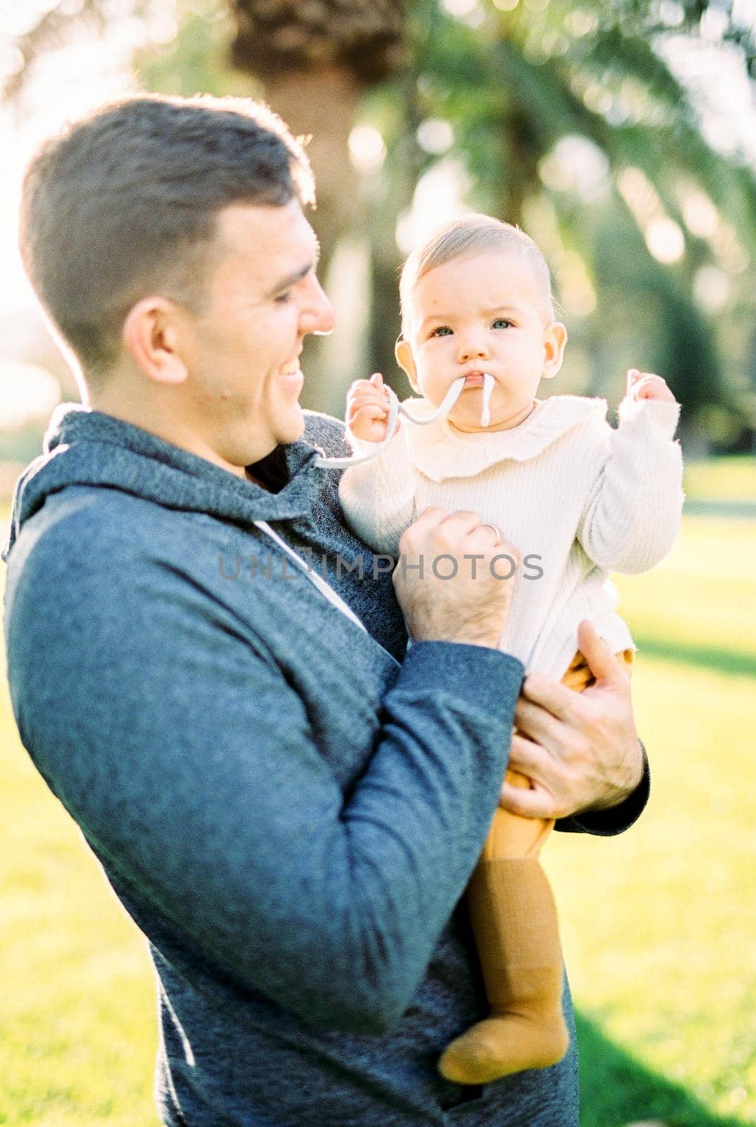 Dad holding a baby chewing on his hoodie string. High quality photo