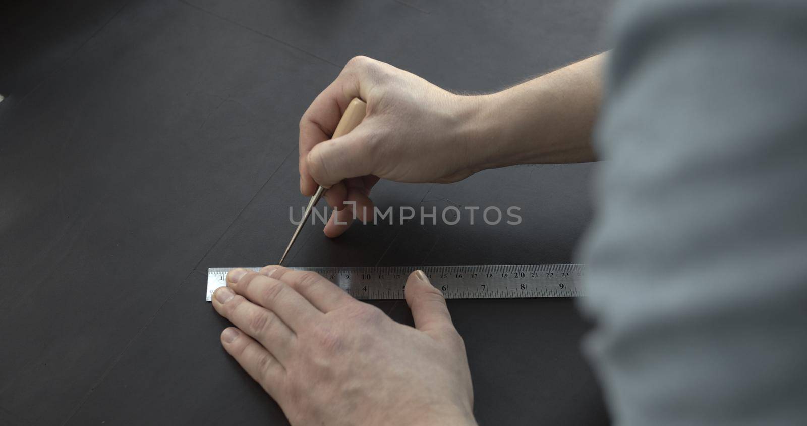 Close up of leather craftsman working with natural leather by awl and ruler. Handmade master at work in local workshop. Leather wallet stitch. by vovsht