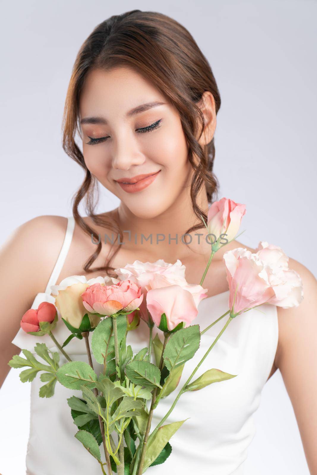 Closeup gorgeous female model with flawless fair skin and perfect makeup holding flowers bouquet. Woman receive flowers, white background.