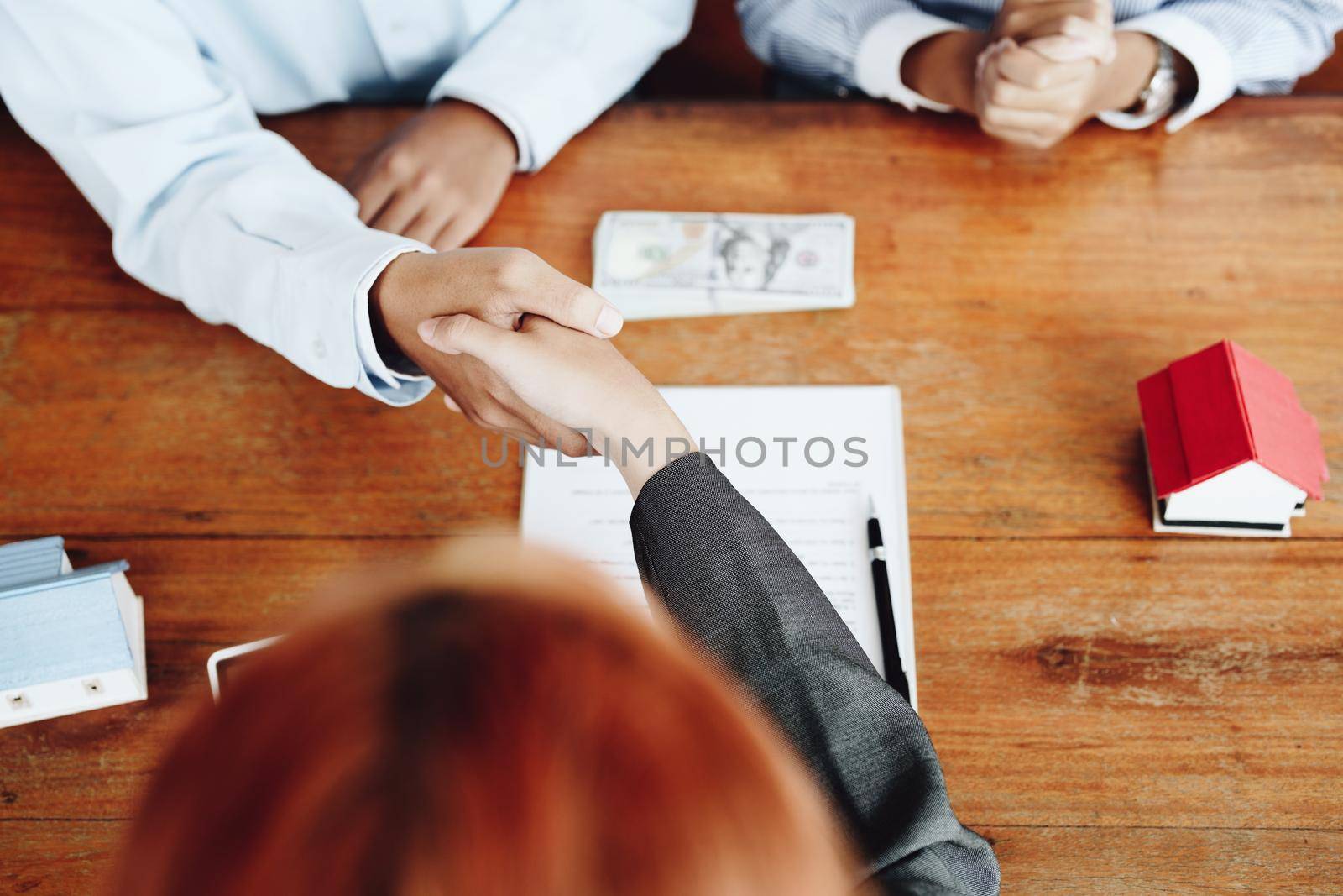 Real estate agents shake hands with customers after signing documents.