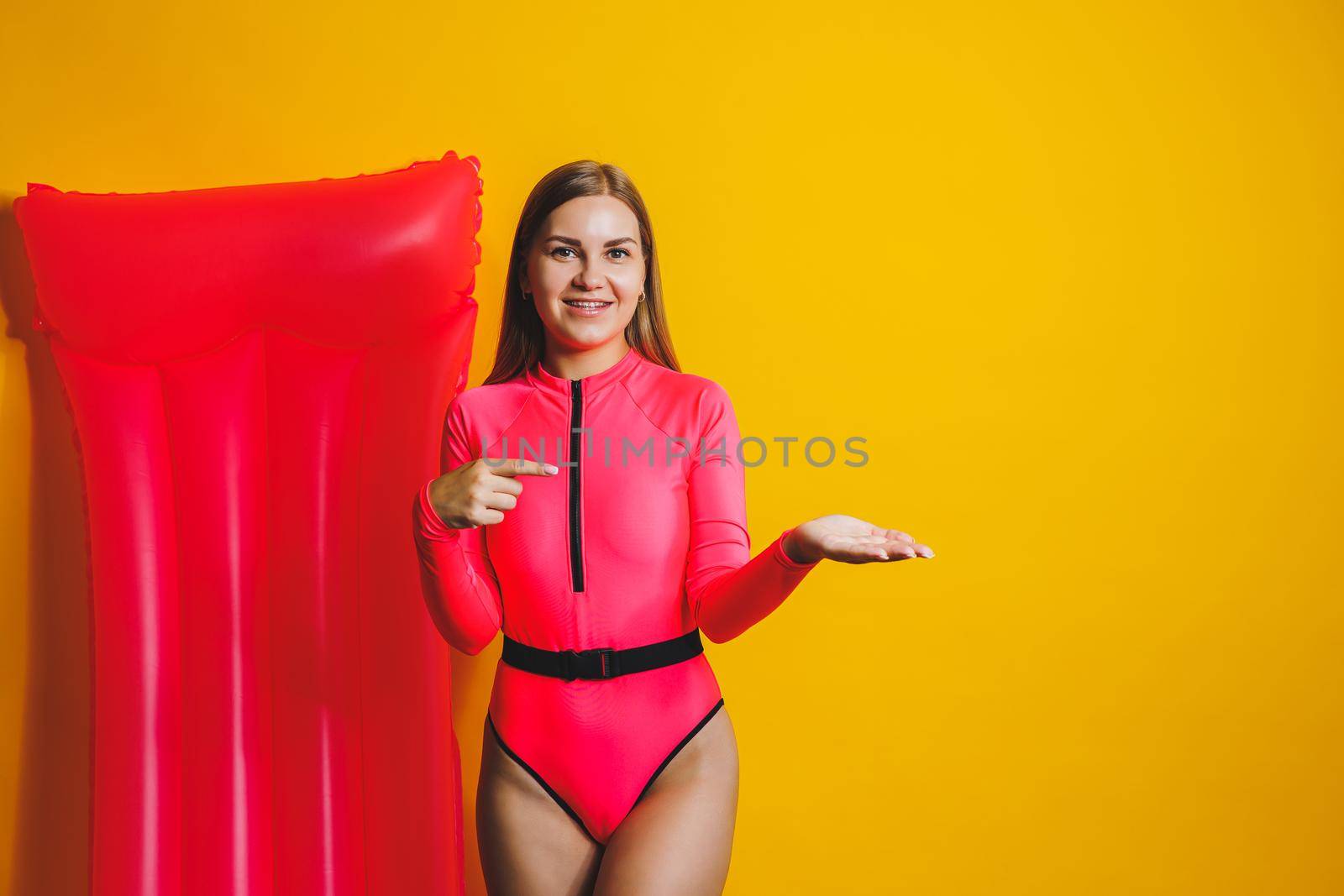 Young woman slim body pink one piece swimsuit on pink air mattress isolated on bright yellow color studio background summer hotel swimming pool sea vacation sun tanning concept. Place for text
