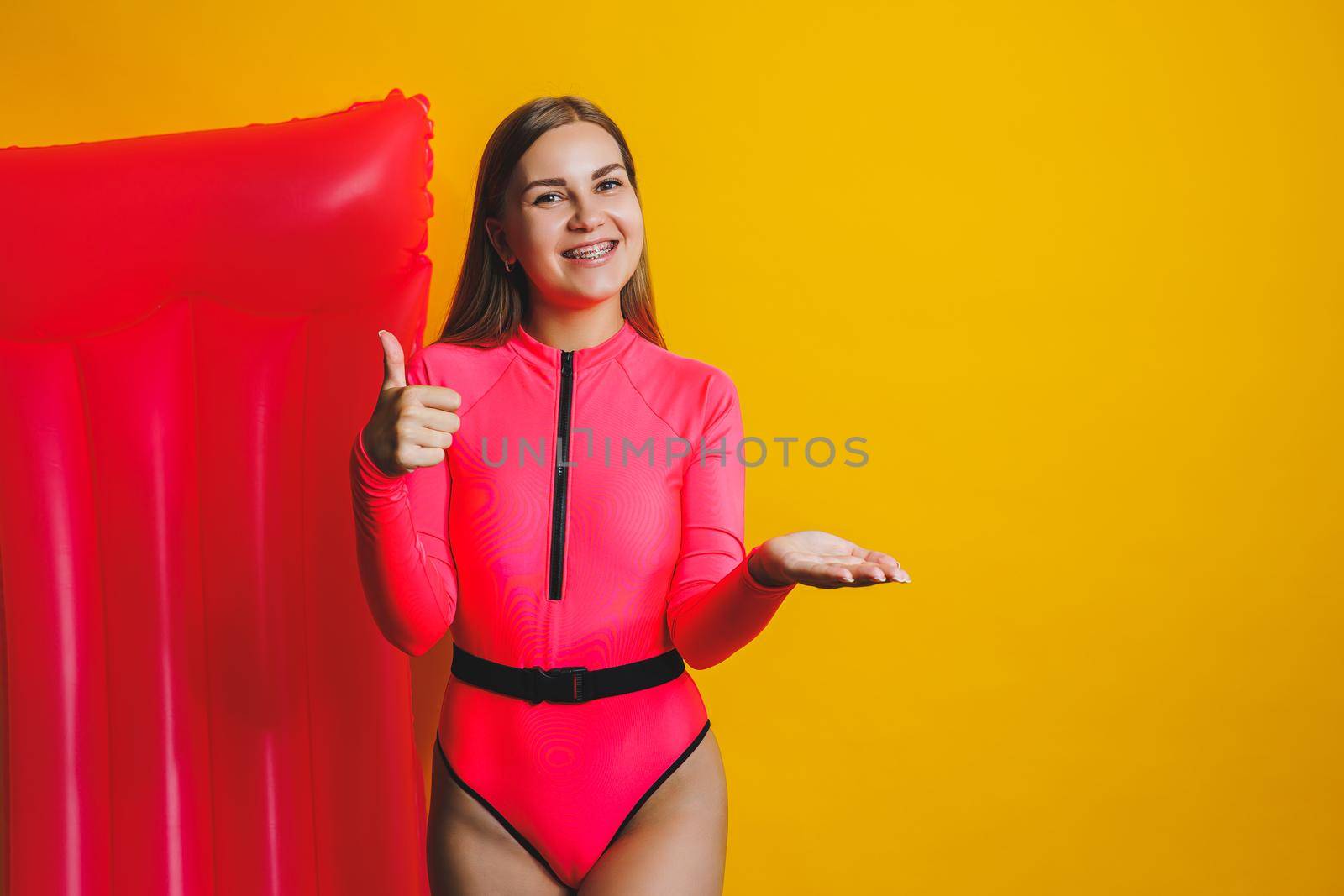 Young woman slim body pink one piece swimsuit on pink air mattress isolated on bright yellow color studio background summer hotel swimming pool sea vacation sun tanning concept. Place for text