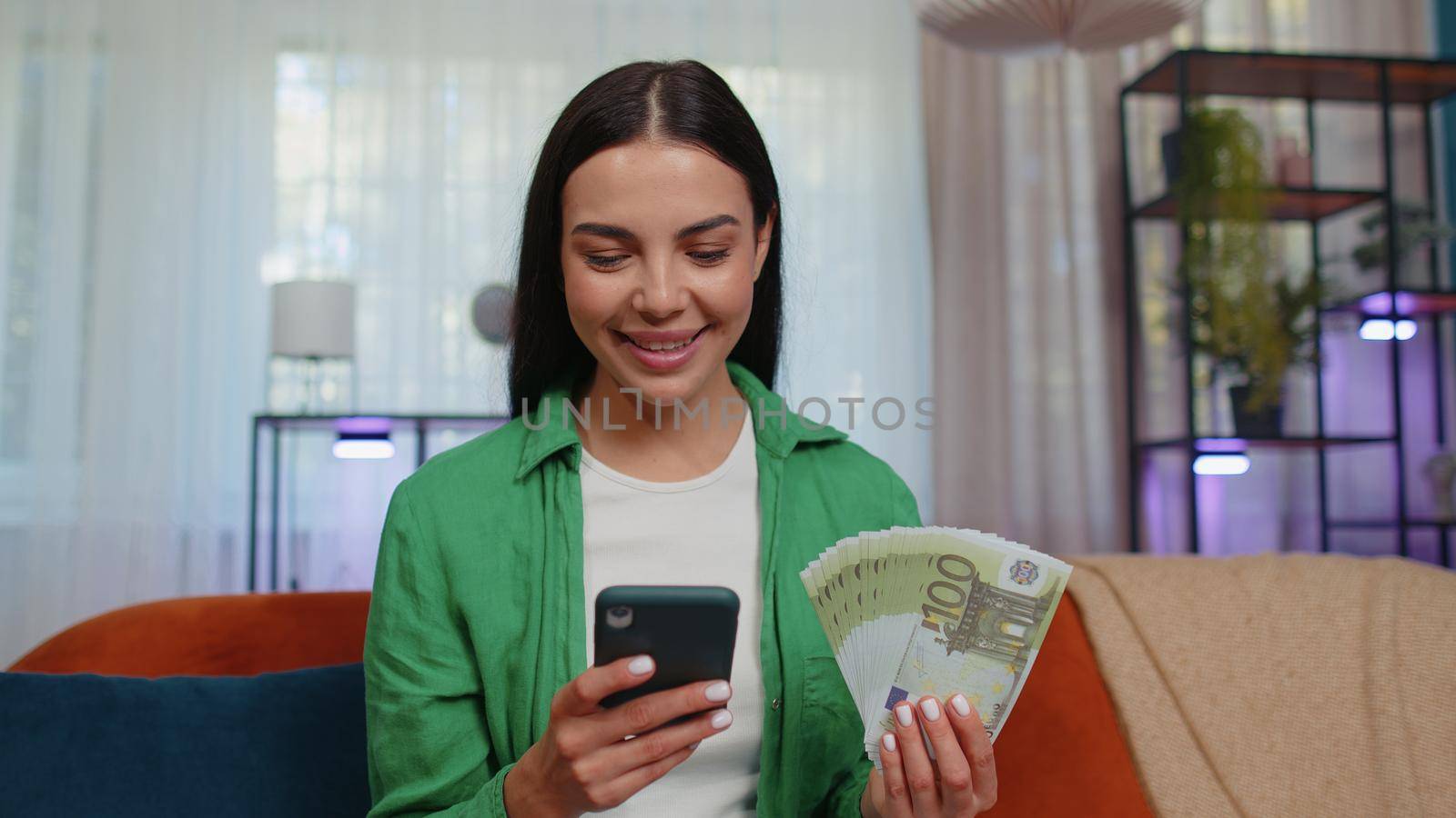 Planning family budget. Smiling caucasian girl counting money euro cash, use smartphone calculate domestic bills at home. Joyful young woman satisfied of income saves money for planned vacation, gifts