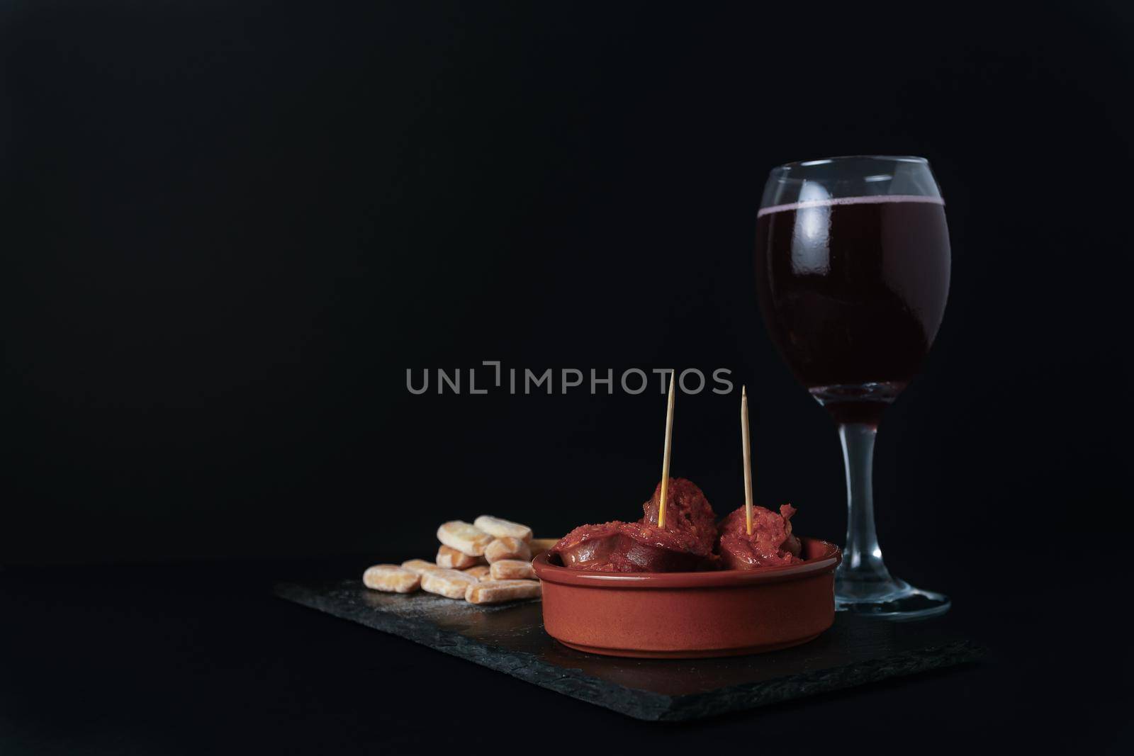 close-up of a tapa of chorizo in sauce, typical Spanish sausage with bread and summer red wine isolated on black background