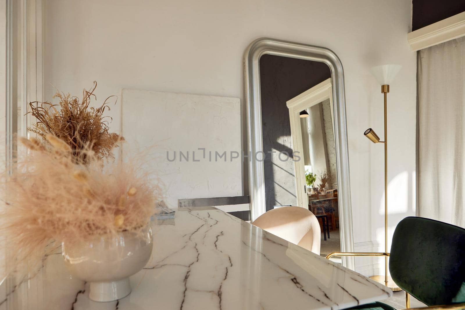 Marble table with feather and grass decorations in vases located near mirror in sunlit elegant room at home