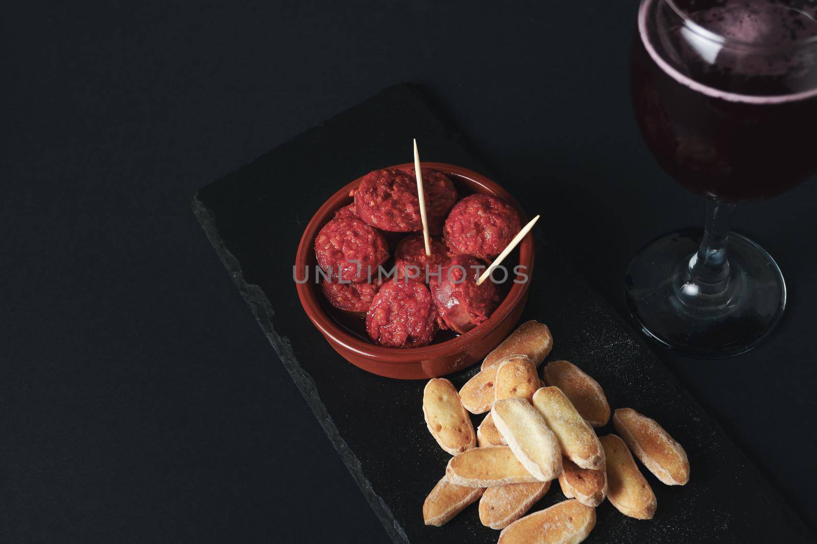 close-up of a tapa of chorizo in sauce, typical Spanish sausage with bread and summer red wine isolated on black background