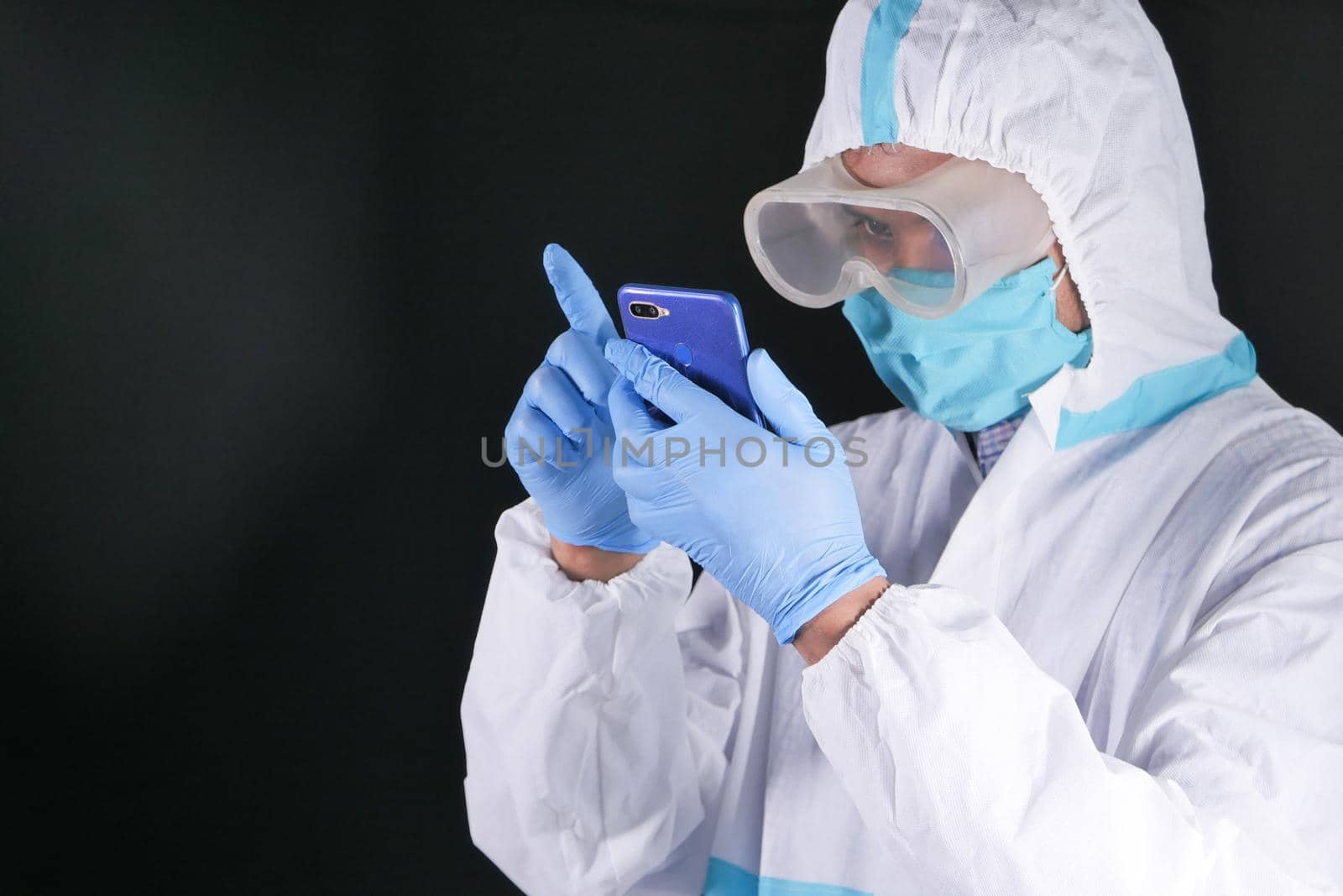 portrait of a male doctor wearing PPE using smart phone .