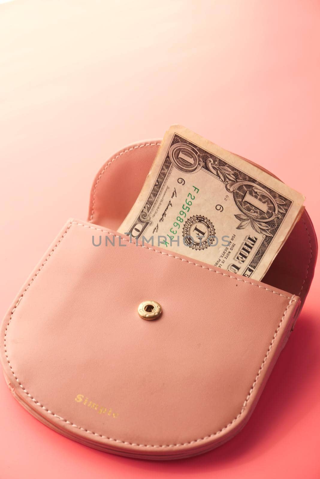 Us dollar cash in a small wallet on pink background .