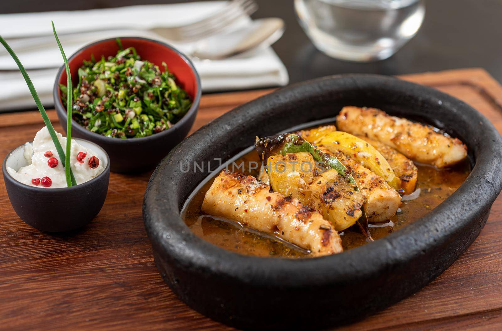 Grilled octopus with quinoa salad on black stone plate.