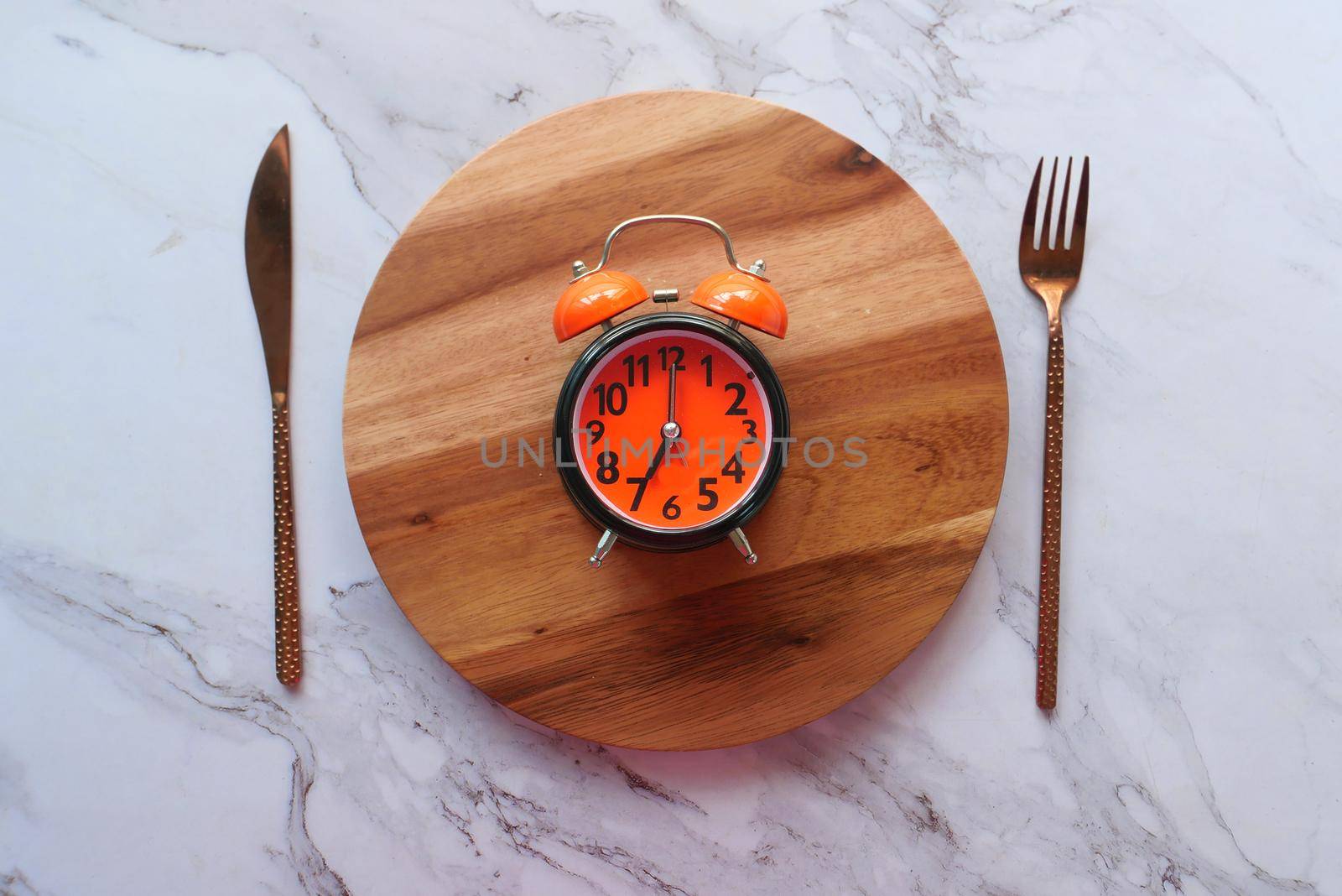 Alarm clock on plate on wooden table, top view