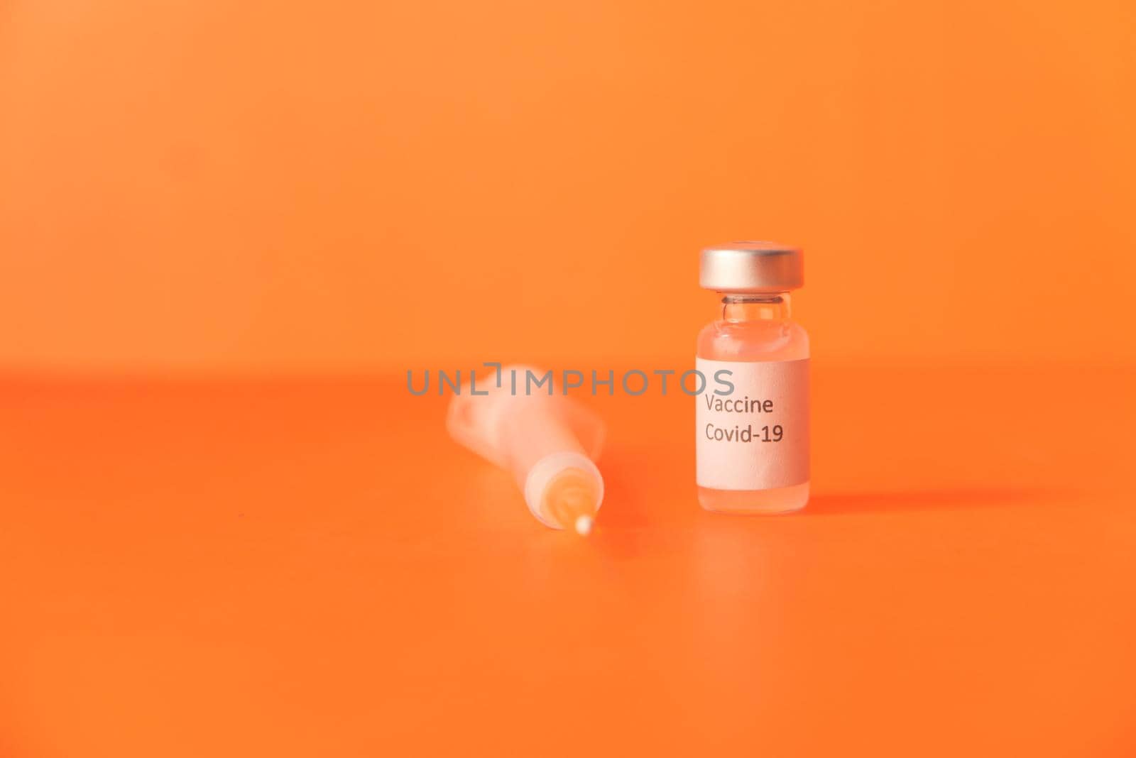 Close up of coronavirus vaccine and syringe on orange background.