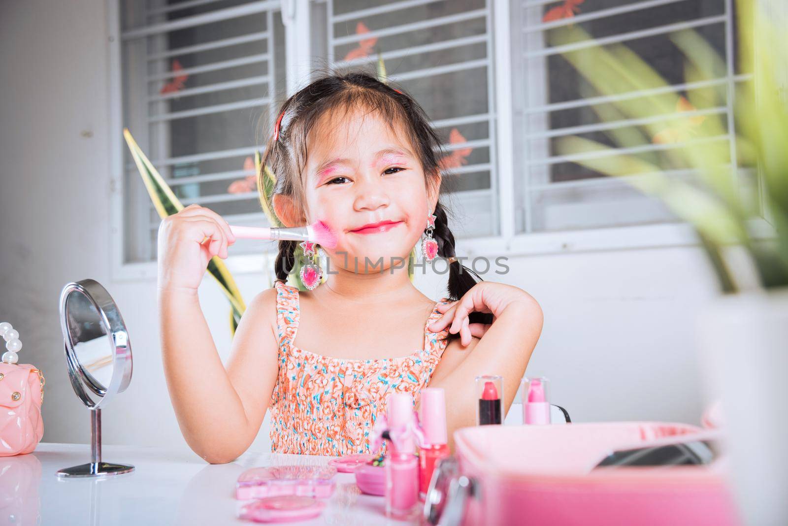 little girl making makeup her face she look in the mirror and cheek fluffy brush for powder by Sorapop