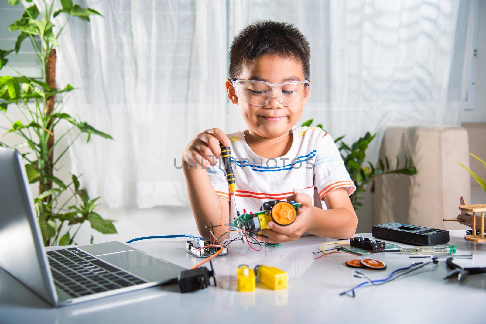 Asian kid boy assembling the Arduino robot car homework project at home by Sorapop