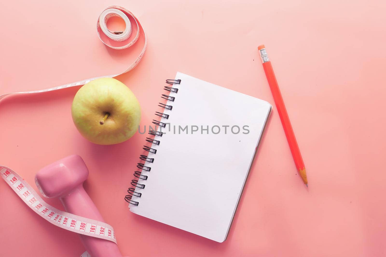 Fitness concept with dumbbell apple and notepad on pink .