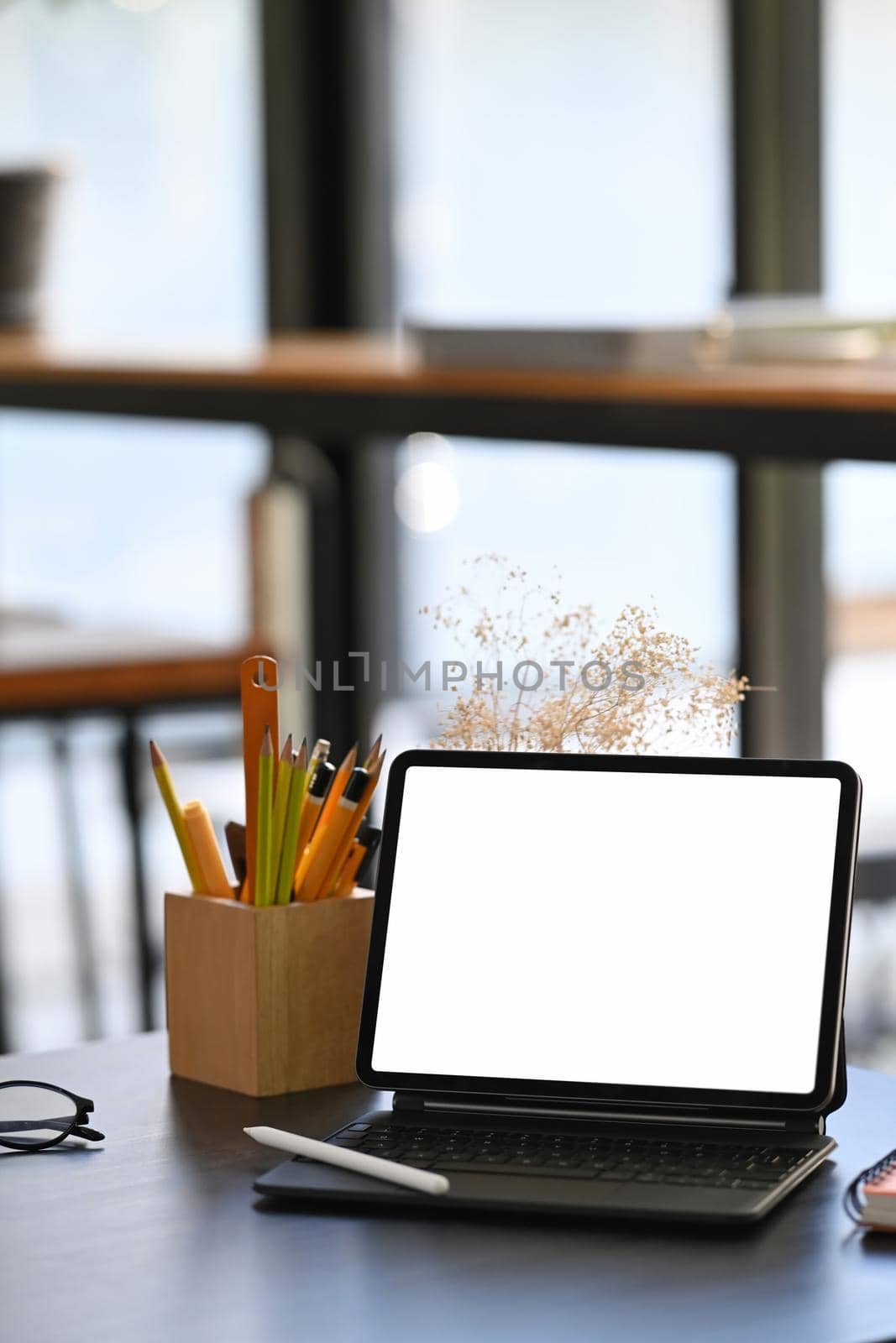 Mock up digital tablet with wireless keyboard and pencil holder on wooden table.