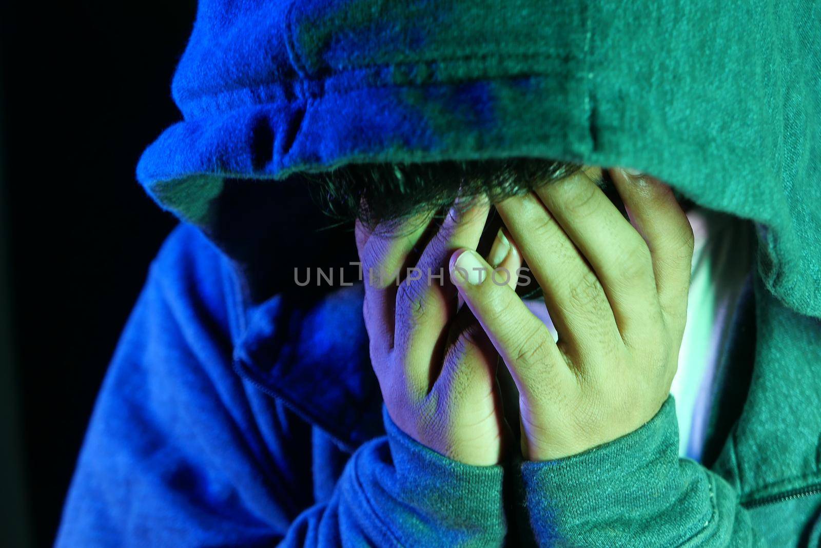 sad man in hood cover face with hands isolated in black