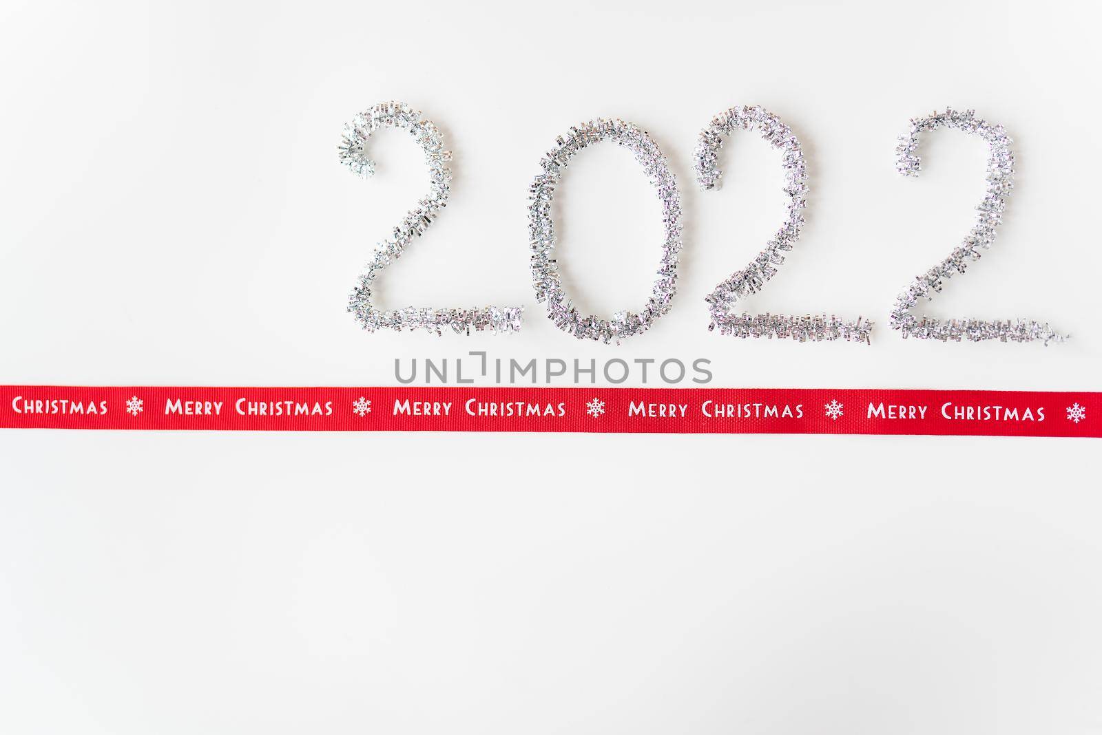 Happy new year 2022 written with foil and new year rain on an isolated white background along with a ribbon with the inscription merry christmas. by sfinks