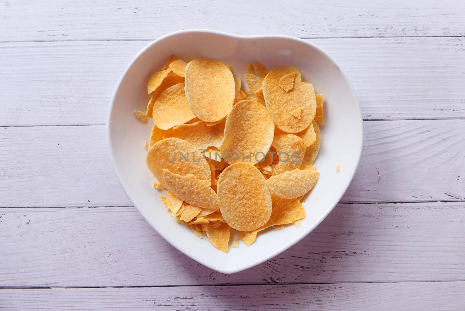 Bowl with tasty potato chips on wooden background