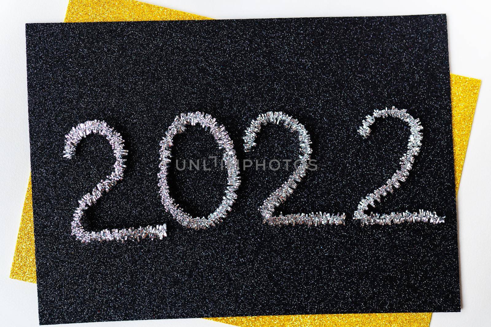 The year 2022 is written in New Year's silver tinsel on a black background. Greeting card