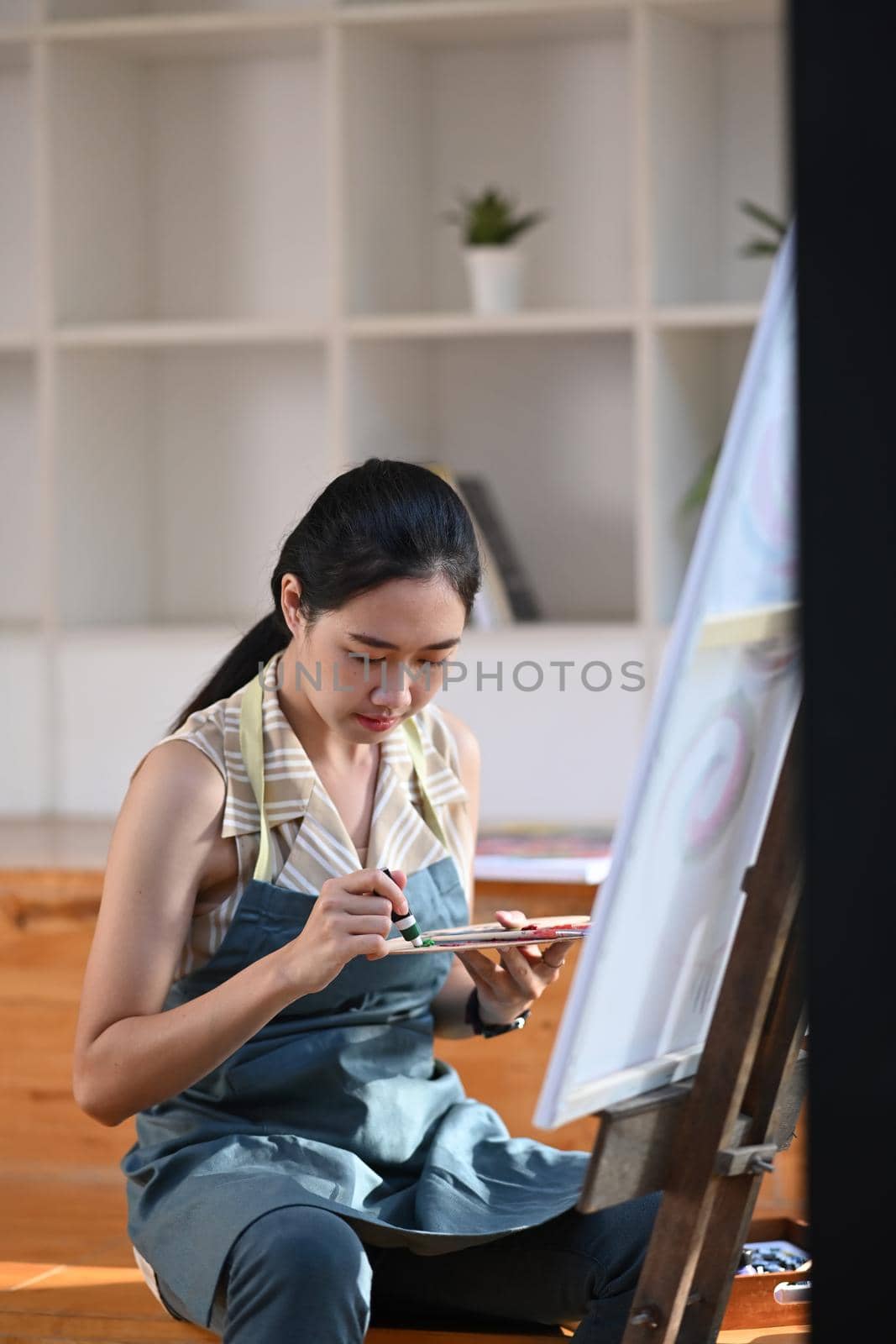 Young asian woman painting on easel in art studio.