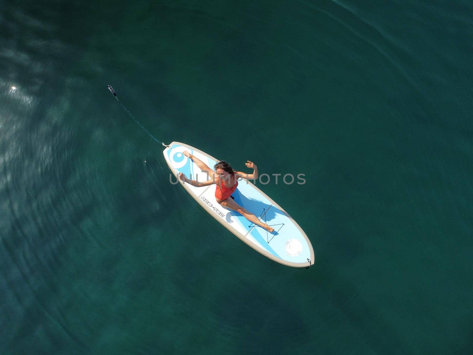 Aerial drone view on well looking middle aged woman with black hair in red swimsuit, swimming on sup in calm azure sea. Summer holiday vacation and travel concept. by panophotograph