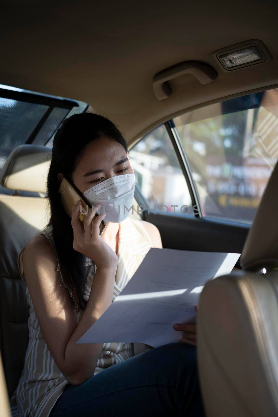 Young business woman talking on mobile phone while sitting in the back seat of the car. by prathanchorruangsak