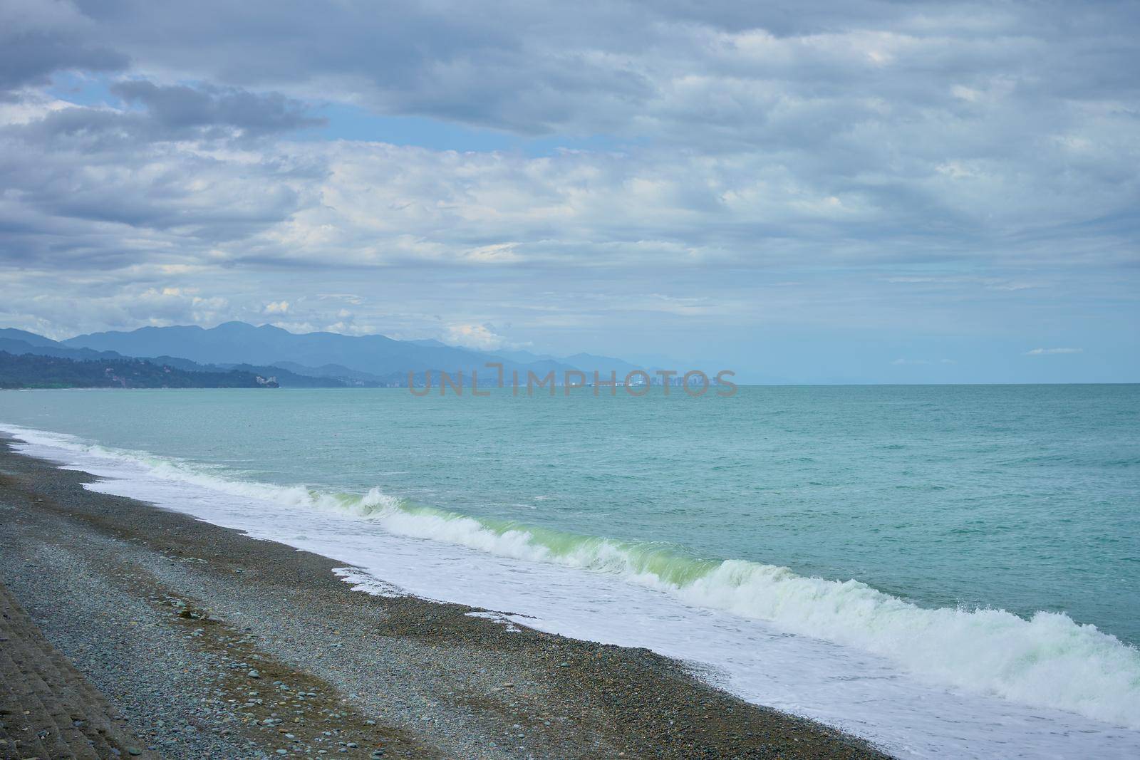 Sea shore with pebbles, wet sea pebbles on the beach and quiet sea surf. Restless sea and waves