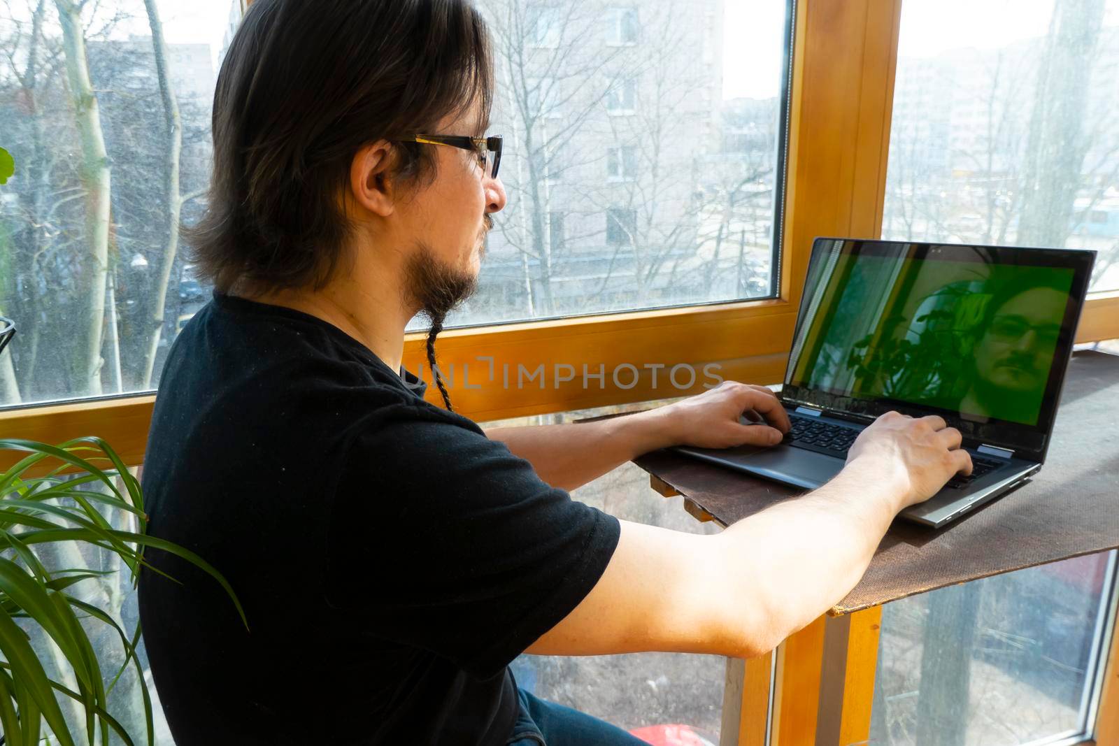 serious man sits on home office and uses a laptop indoors. home office on the balcony. freelancing and remote work concept